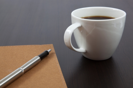 Cup of coffee on a wooden table with book and penの写真素材