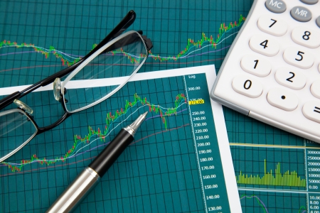 A pen, calculator and spectacles on the Stock chart and financial reportの写真素材