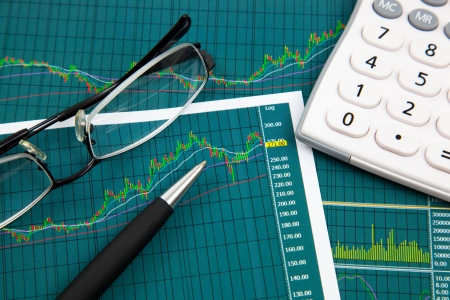 A pen, calculator and spectacles on the Stock chart and financial reportの写真素材