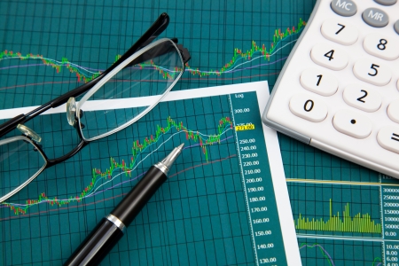 A pen, calculator and spectacles on the Stock chart and financial reportの写真素材