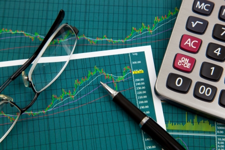 A pen, calculator and spectacles on the Stock chart and financial reportの写真素材