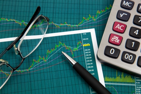 A pen, calculator and spectacles on the Stock chart and financial reportの写真素材