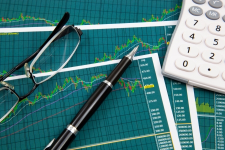 A pen, calculator and spectacles on the Stock chart and financial reportの写真素材