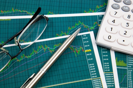 A pen, calculator and spectacles on the Stock chart and financial reportの写真素材