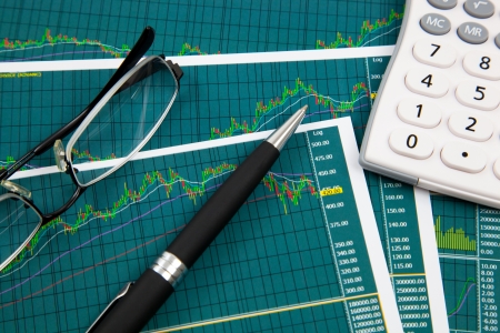 A pen, calculator and spectacles on the Stock chart and financial reportの写真素材