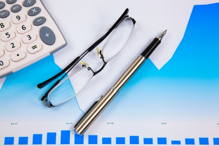 A pen, calculator and spectacles on the Stock chart and financial reportの写真素材