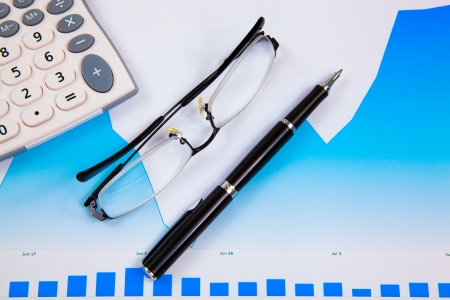 A pen, calculator and spectacles on the Stock chart and financial reportの写真素材