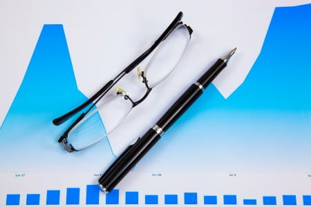 A pen and spectacles on the Stock chart and financial reportの写真素材