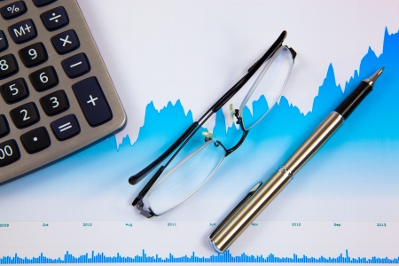 A pen, calculator and spectacles on the Stock chart and financial reportの写真素材
