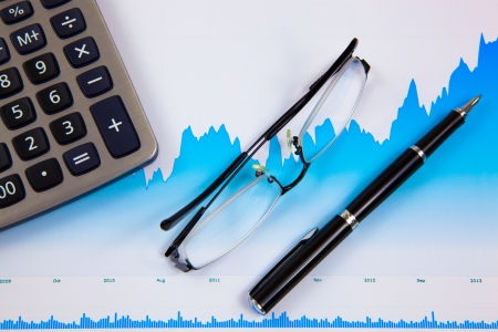 A pen, calculator and spectacles on the Stock chart and financial reportの写真素材