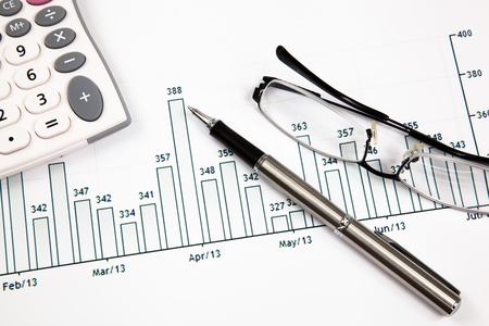 A pen, calculator and spectacles on the Stock chart and financial reportの写真素材
