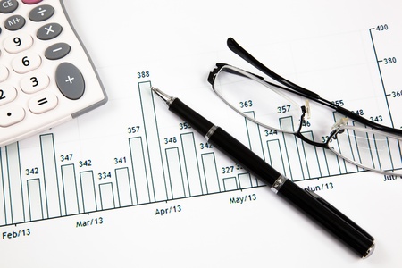 A pen, calculator and spectacles on the Stock chart and financial reportの写真素材