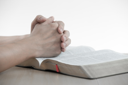 hands praying with bible on table