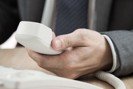 Male hand holding phone receiver over telephoneの写真素材
