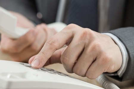 Male hand holding phone receiver over telephoneの写真素材