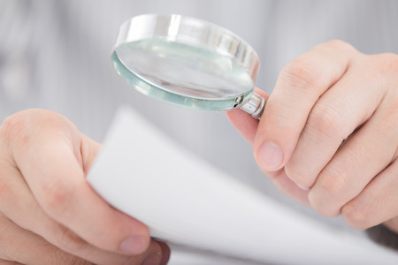 Businessman looking through a magnifying glass to documentsの写真素材
