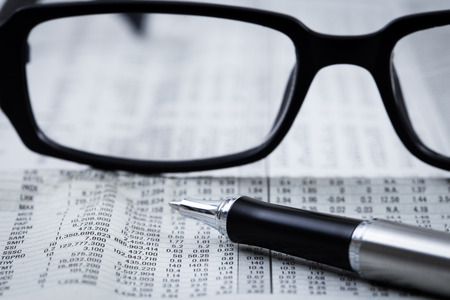 closeup glasses on financial newspaper with penの写真素材
