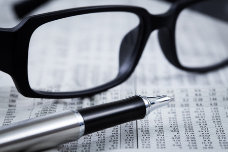 closeup glasses on financial newspaper with penの写真素材
