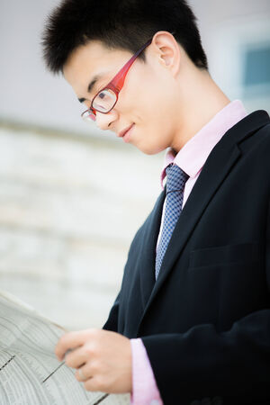 A young businessman reading newspaper outdoorsの写真素材