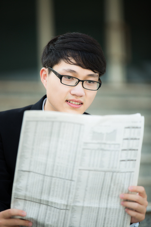 A young businessman reading newspaper outdoorsの写真素材