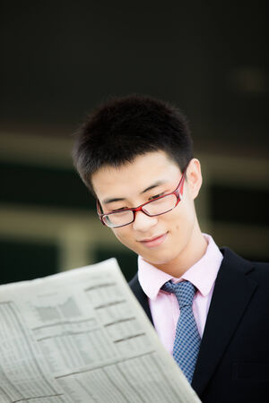A young businessman reading newspaper outdoorsの写真素材