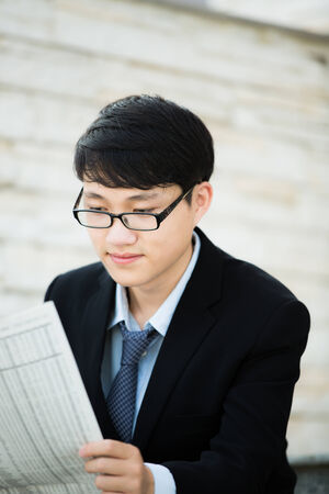 A young businessman reading newspaper outdoorsの写真素材