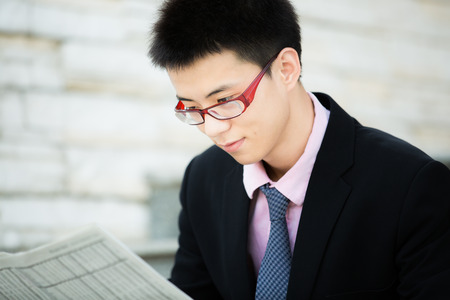 A young businessman reading newspaper outdoorsの写真素材