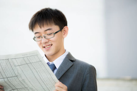 A young businessman reading newspaper outdoorsの写真素材
