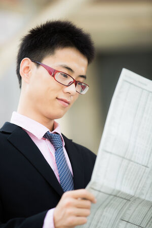 A young businessman reading newspaper outdoorsの写真素材