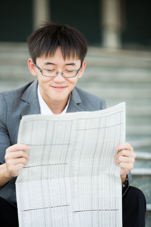 A young businessman reading newspaper outdoorsの写真素材