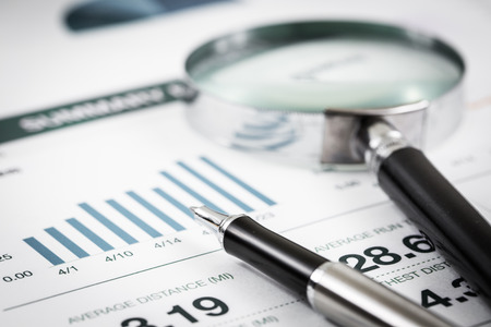 magnifying glass and pen over graph on tableの写真素材
