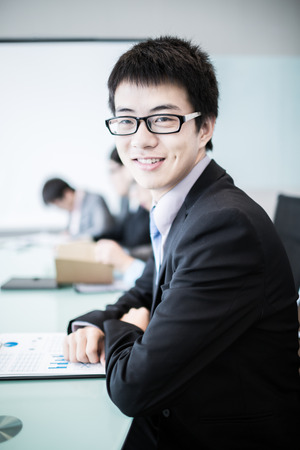 Businessman smiling at the camera while his team is working in the background.Asianの写真素材