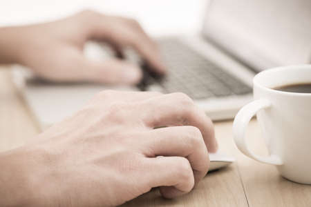 Hands of a man working with laptop and cup of coffeeの写真素材