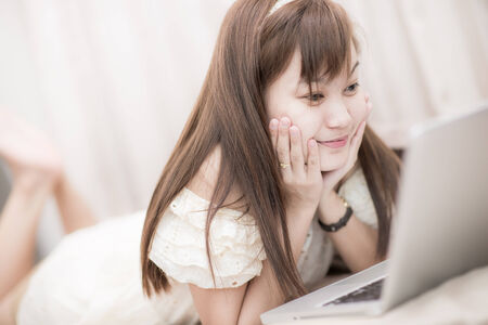 happy brunette woman with a laptop in the bed at homeの写真素材