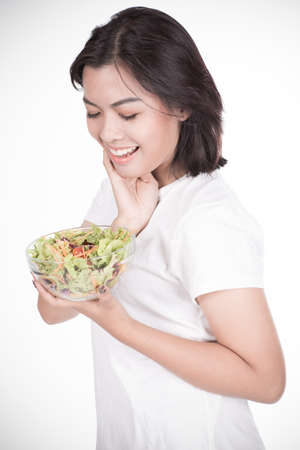 Portrait of a fit healthy hispanic woman eating a fresh salad isolated on whiteの写真素材