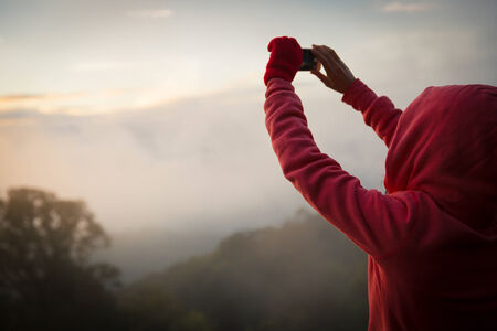 woman hiker taking photo with smart phone at mountain peak