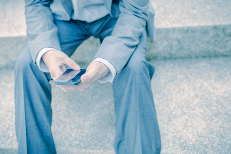 Young businessman using a phone sitting on the stairsの写真素材