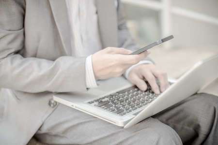 Businessman using laptop pc and mobile phone. He is sitting on a stairs.の写真素材