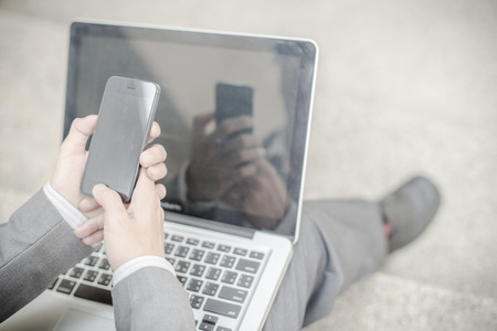 Businessman using laptop pc and mobile phone. He is sitting on a stairs.の写真素材