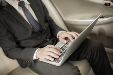 Young business using laptop in back seat of carの写真素材