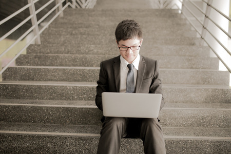 Young man sitting on the stairs using laptopの写真素材