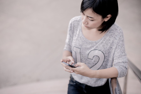 female university student using mobile on stairsの写真素材