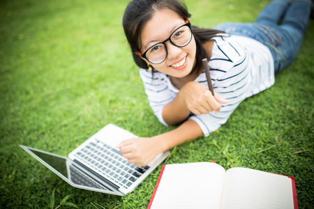 Young female on grass with laptop and books doing a homeworkの写真素材