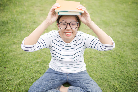 A female college student reading a book while lying on the parkの写真素材