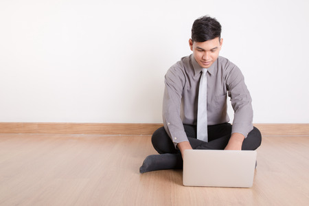 Young businessman sitting on the floor and typing on a laptopの写真素材