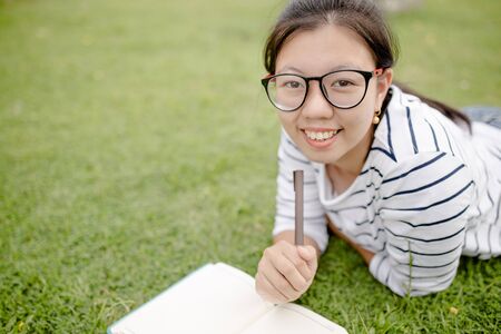 A female college student reading a book while lying on the parkの写真素材