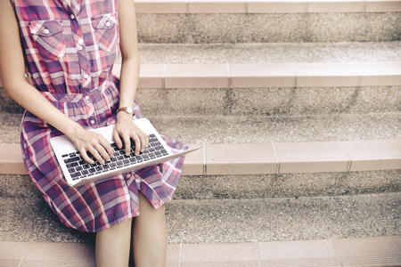female university student using mobile on stairsの写真素材