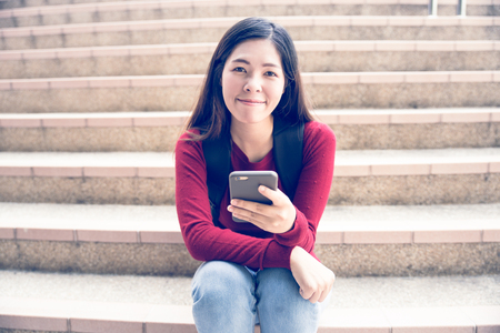 Asian beautiful female student using mobile phone on stepsの写真素材