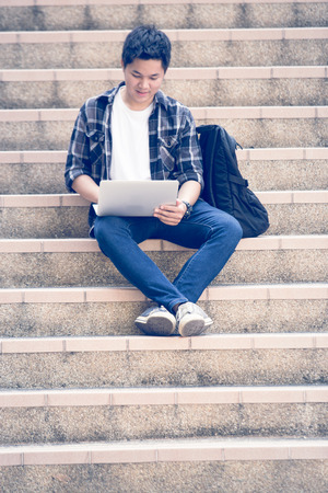Young man sitting on the stairs using laptopの写真素材