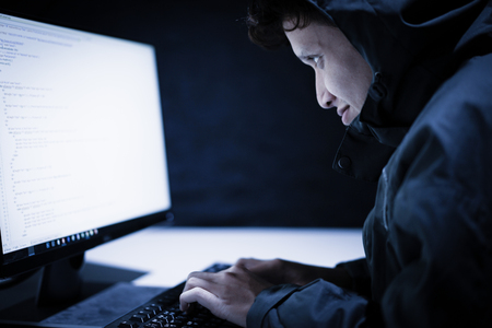 Hooded computer hacker stealing information with laptopの写真素材